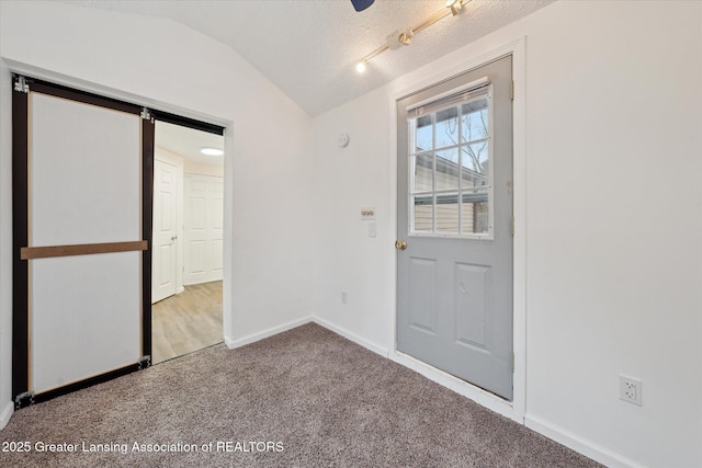 interior space with a barn door, baseboards, carpet, vaulted ceiling, and a textured ceiling