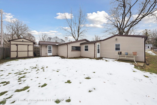 snow covered back of property featuring a garage, an outbuilding, fence, and a shed