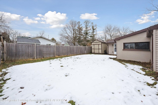 yard covered in snow with a fenced backyard, an outdoor structure, and a storage unit