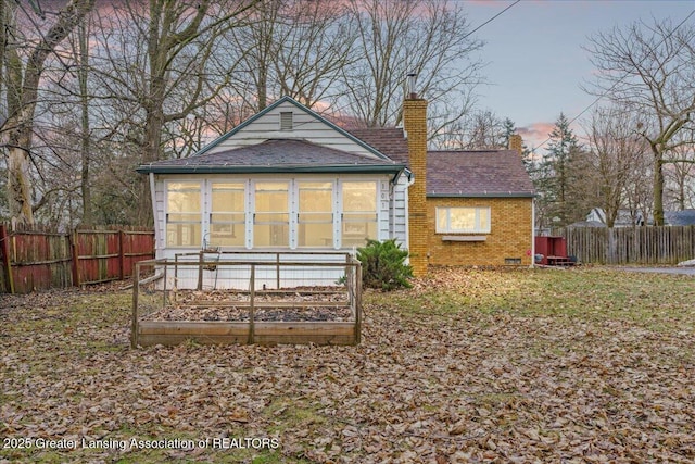 rear view of house featuring brick siding, a chimney, a vegetable garden, and fence