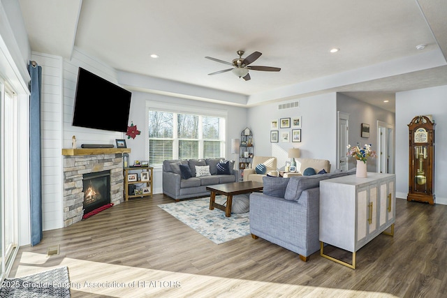 living room with a ceiling fan, a fireplace, visible vents, and wood finished floors