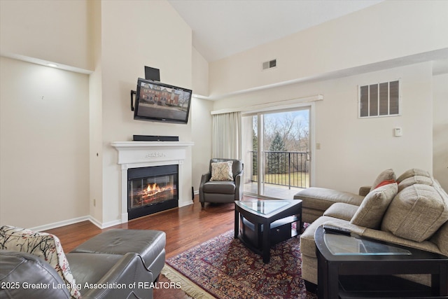 living area featuring high vaulted ceiling, visible vents, wood finished floors, and a glass covered fireplace