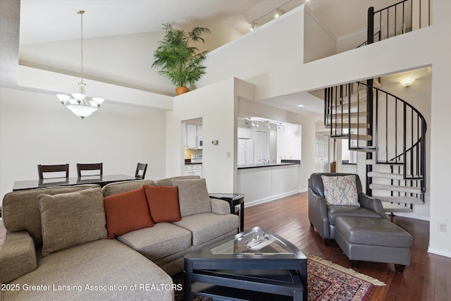 living room featuring a notable chandelier, wood-type flooring, high vaulted ceiling, baseboards, and stairs