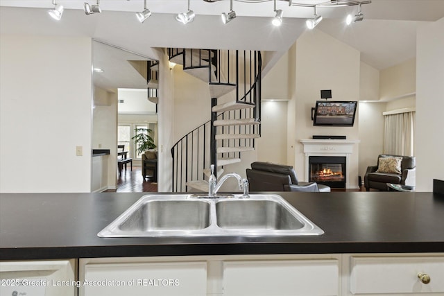 kitchen with dark countertops, open floor plan, a sink, and a glass covered fireplace