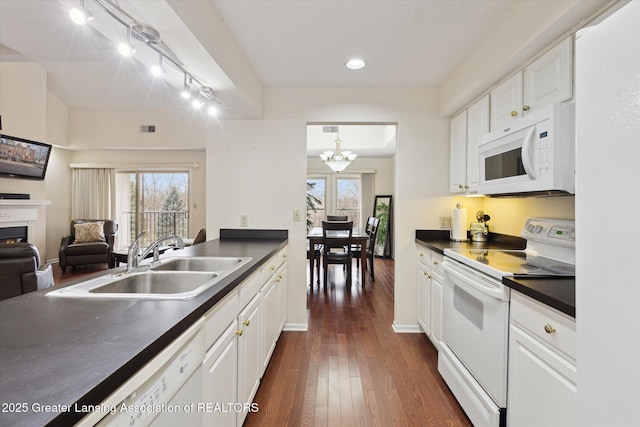 kitchen featuring white appliances, a sink, white cabinetry, a lit fireplace, and dark countertops