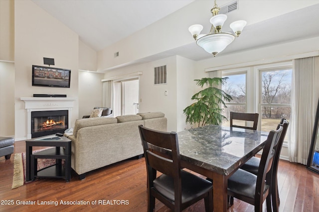 dining space with a glass covered fireplace, visible vents, dark wood finished floors, and an inviting chandelier