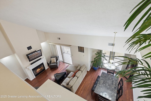 living area featuring lofted ceiling, wood finished floors, a glass covered fireplace, and visible vents