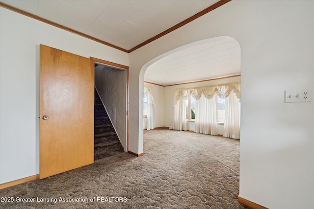 carpeted empty room with arched walkways, crown molding, baseboards, and stairs