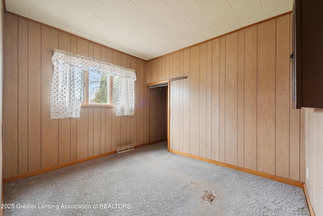 carpeted spare room featuring visible vents, wooden walls, and baseboards