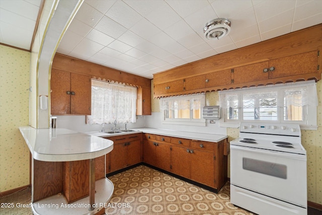 kitchen featuring light countertops, electric range, brown cabinets, and wallpapered walls