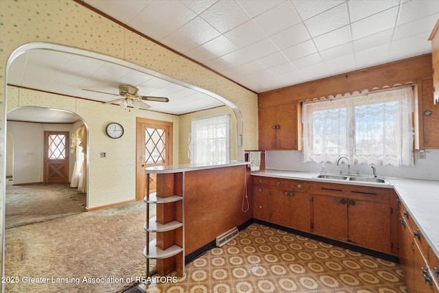 kitchen featuring arched walkways, light countertops, visible vents, a sink, and wallpapered walls