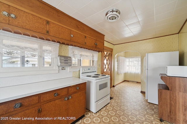 kitchen with arched walkways, white appliances, brown cabinets, and wallpapered walls