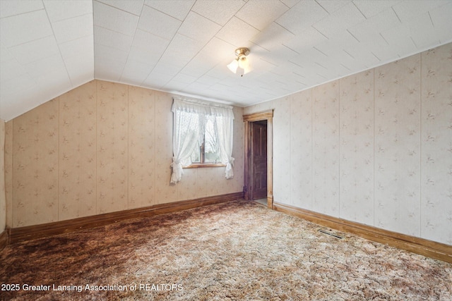 carpeted spare room with lofted ceiling, visible vents, baseboards, and wallpapered walls