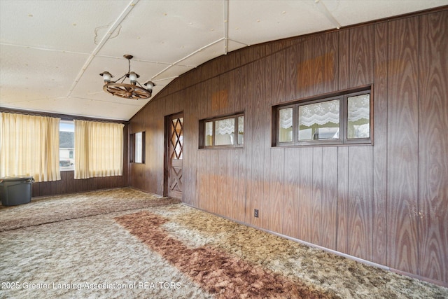 empty room featuring carpet floors, lofted ceiling, a notable chandelier, and wood walls