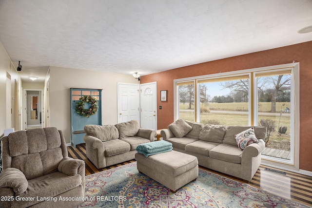 living room with baseboards, a textured ceiling, visible vents, and wood finished floors