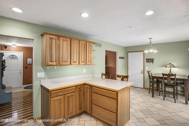 kitchen with decorative light fixtures, recessed lighting, light countertops, visible vents, and a peninsula