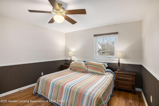 bedroom with ceiling fan, wood walls, wainscoting, and wood finished floors