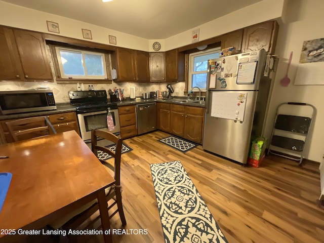 kitchen featuring stainless steel appliances, a sink, light wood finished floors, dark countertops, and tasteful backsplash