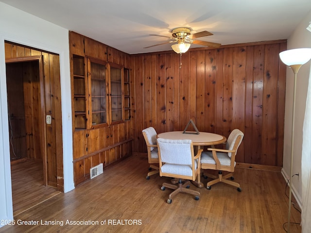 dining area featuring visible vents, ceiling fan, wood walls, and wood finished floors