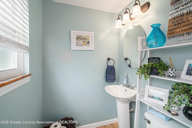 half bathroom featuring a notable chandelier, toilet, and baseboards