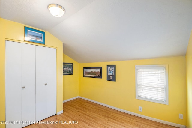 unfurnished bedroom with a closet, baseboards, vaulted ceiling, and wood finished floors