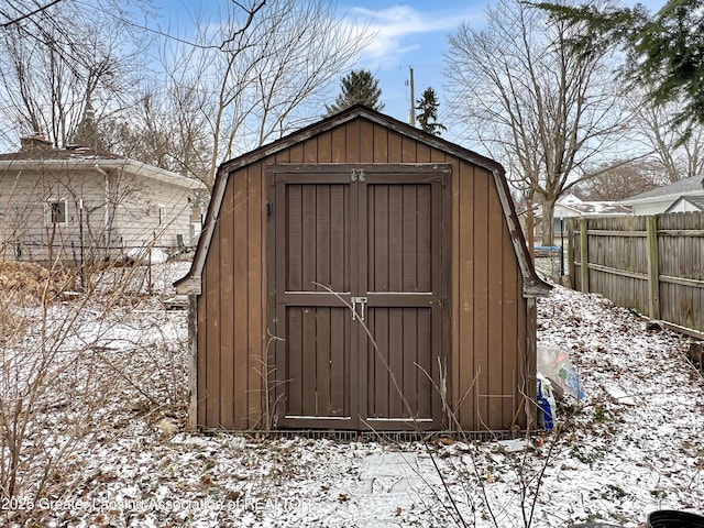 snow covered structure featuring a storage shed, fence, and an outdoor structure