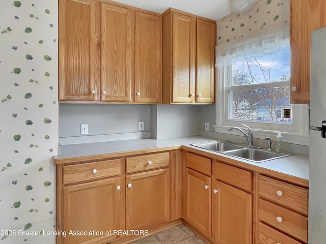 kitchen featuring wallpapered walls, light countertops, and a sink