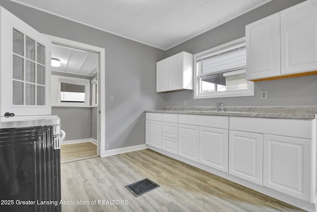 kitchen with light wood finished floors, visible vents, baseboards, light countertops, and white cabinetry