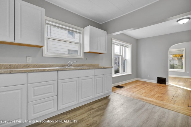 kitchen featuring light wood-type flooring, light countertops, arched walkways, white cabinetry, and a sink