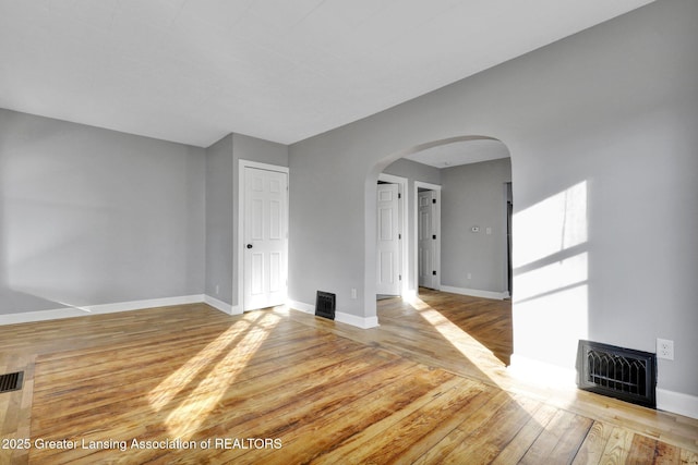 unfurnished living room with baseboards, arched walkways, visible vents, and wood finished floors