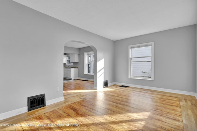 unfurnished room featuring visible vents, baseboards, a fireplace, hardwood / wood-style flooring, and arched walkways