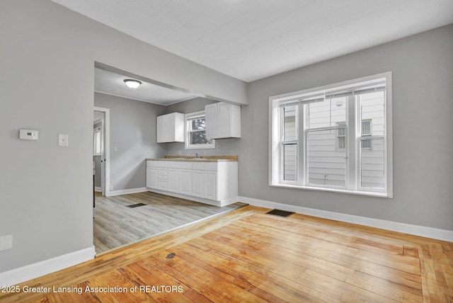 kitchen with baseboards, visible vents, light wood-style flooring, a sink, and white cabinets