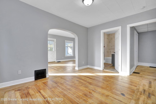 empty room with baseboards, visible vents, arched walkways, and light wood-type flooring