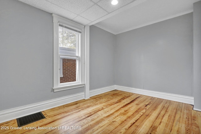 empty room featuring wood finished floors, crown molding, baseboards, and visible vents