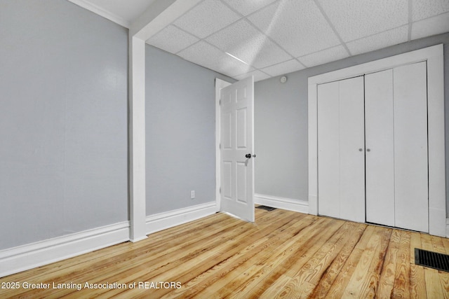 unfurnished bedroom featuring visible vents, baseboards, a drop ceiling, wood finished floors, and a closet