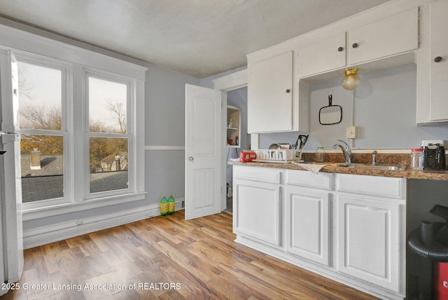 kitchen with baseboards, stone counters, light wood-style flooring, a sink, and white cabinetry