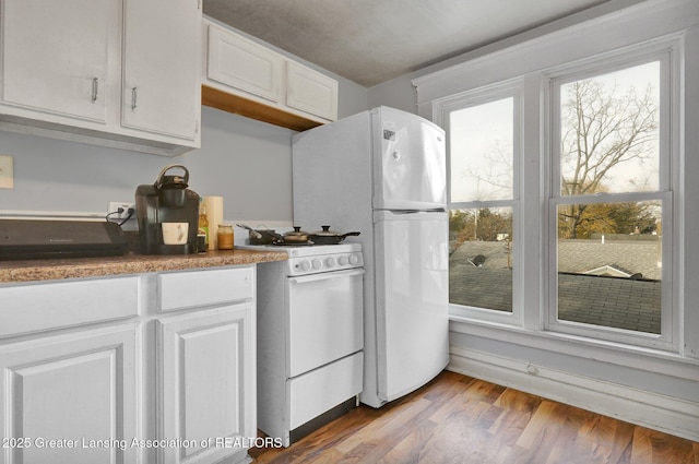 kitchen with a healthy amount of sunlight, white appliances, white cabinets, and wood finished floors