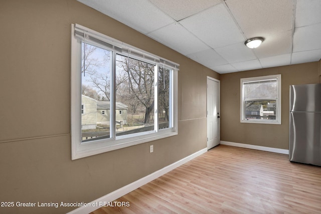 empty room featuring light wood finished floors, baseboards, and a drop ceiling