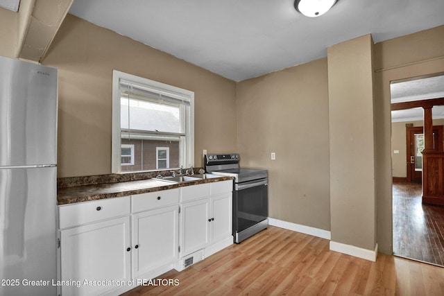 kitchen featuring white cabinets, dark countertops, appliances with stainless steel finishes, light wood-type flooring, and a sink