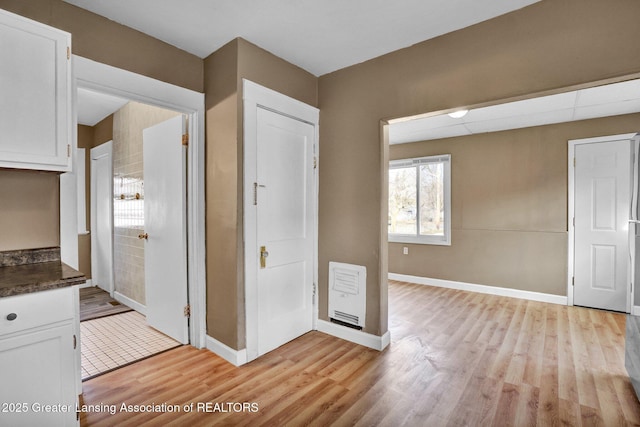 interior space featuring light wood-type flooring, white cabinetry, dark countertops, and baseboards