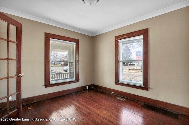 empty room with crown molding, visible vents, dark wood finished floors, and baseboards