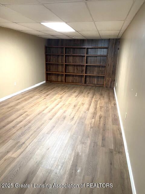 spare room with light wood-style floors, a drop ceiling, and baseboards