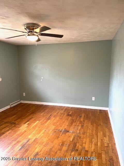 unfurnished room featuring hardwood / wood-style flooring, baseboards, a baseboard heating unit, and ceiling fan