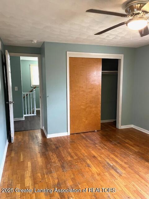 unfurnished bedroom with a closet, wood-type flooring, baseboards, and a ceiling fan