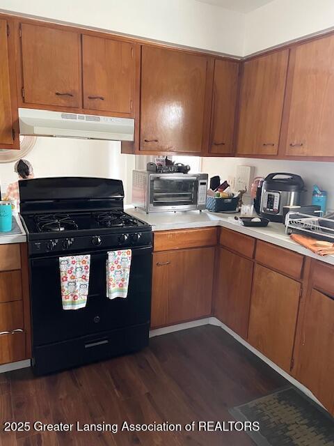 kitchen with under cabinet range hood, black range with gas stovetop, light countertops, and dark wood-type flooring