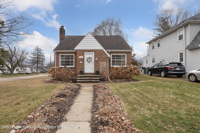 view of front of home with a shingled roof, a chimney, a front lawn, and brick siding