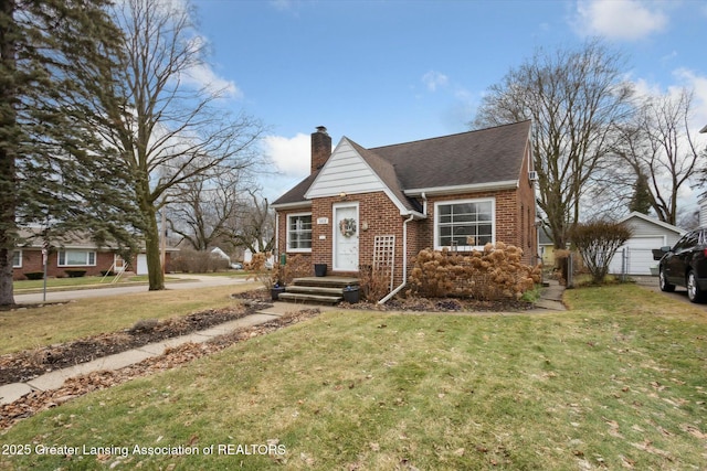 view of front facade with brick siding, a chimney, a shingled roof, a front yard, and an outdoor structure