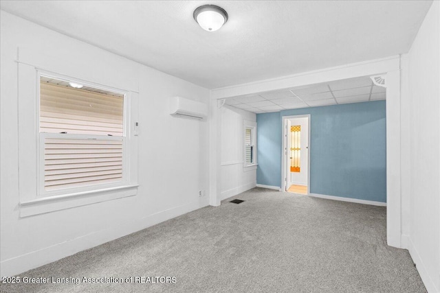 carpeted empty room featuring a drop ceiling, a wall mounted air conditioner, and baseboards