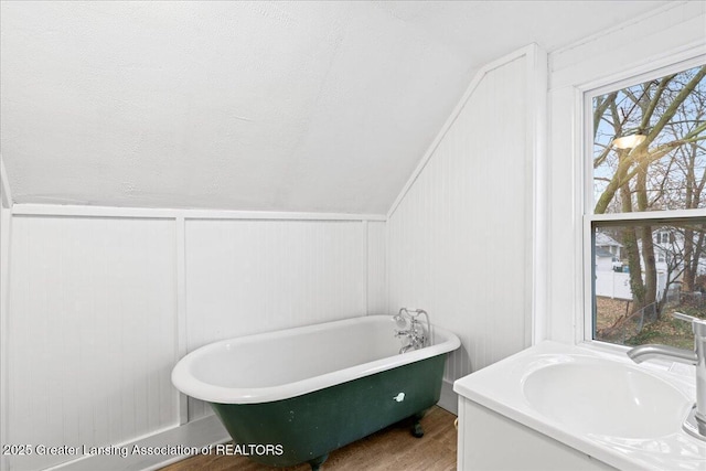 bathroom featuring lofted ceiling, a sink, a soaking tub, and wood finished floors