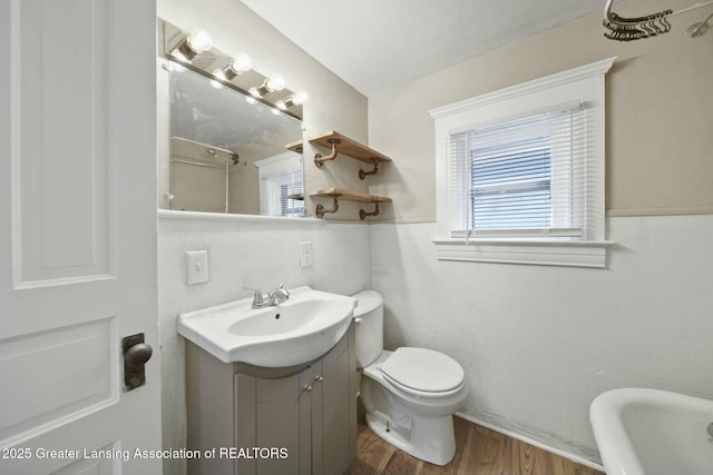 full bath with toilet, wood finished floors, vanity, tile walls, and a tub